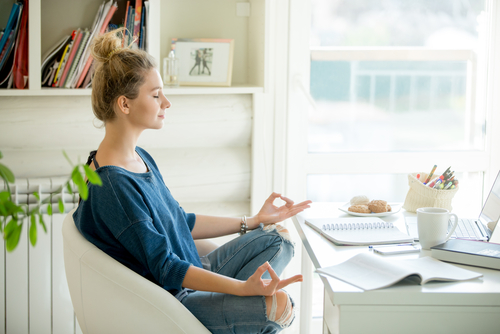 A woman meditates sitting in a chair at her desk
